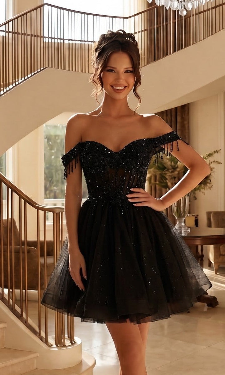 Woman wearing the Short Champagne Corset Prom Dress: Juliet JT947L in black, featuring an off-the-shoulder tulle design with a corset-style bodice and beaded fringe, standing indoors by a staircase.